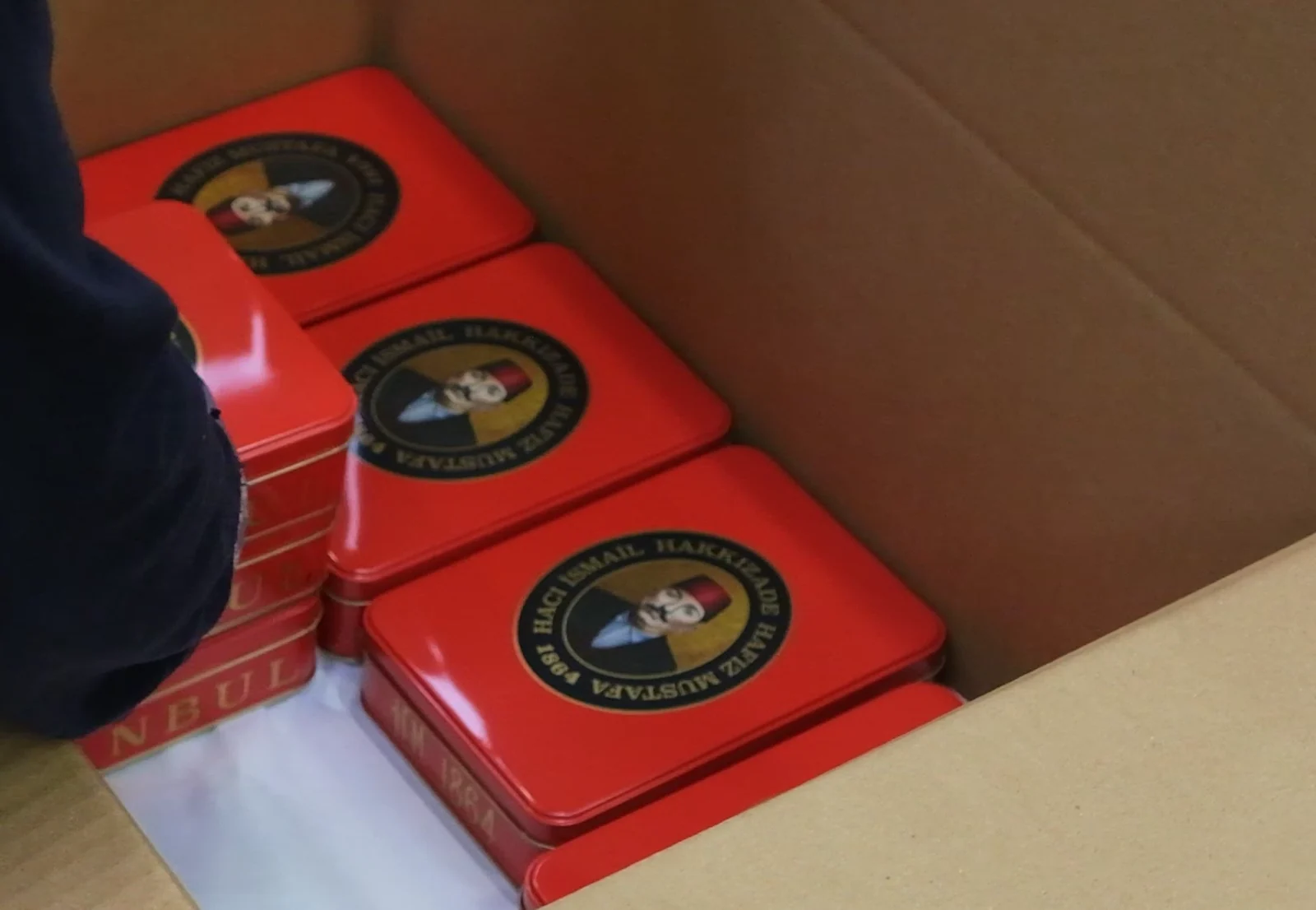 Hands packing finished decorative tins for shipment